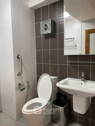 Modern bathroom with sleek fixtures and textured tiles, featuring a toilet, sink, and safety handrail.