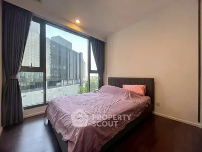 Modern bedroom with large window and city view, featuring elegant curtains and cozy bed setup.