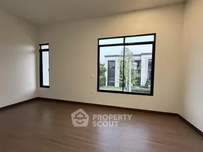 Spacious empty room with large window offering a view of modern architecture and greenery.