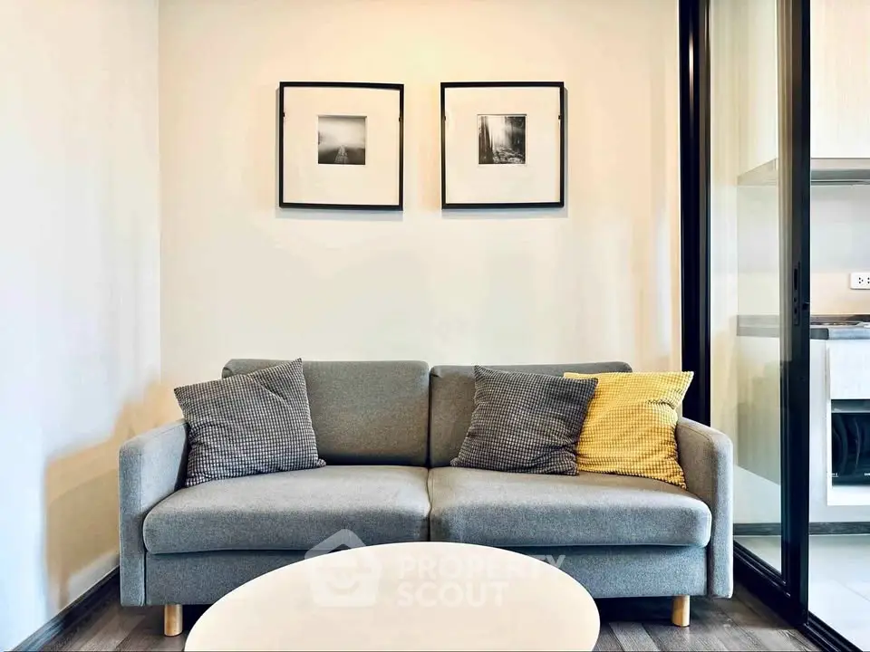 Modern living room with stylish gray sofa and decorative pillows, framed art on wall, and sleek glass partition.
