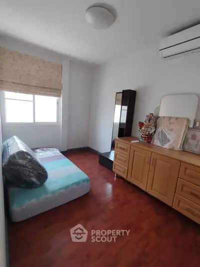 Cozy bedroom with wooden flooring, air conditioning, and ample natural light from a large window.