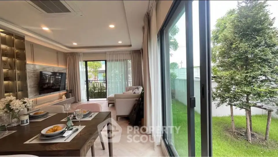 Spacious living room with large windows and garden view, featuring modern decor and dining area.