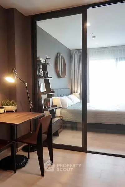 Modern bedroom with glass partition and cozy study area, featuring stylish decor and natural light.