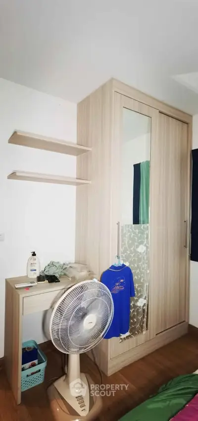 Cozy bedroom corner with wardrobe, fan, and small desk, perfect for compact living spaces.