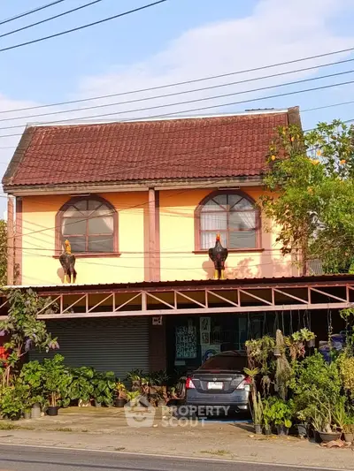 Charming two-story house with unique rooster statues and lush greenery in front, perfect for nature lovers.