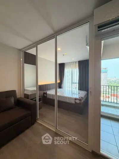 Modern bedroom with mirrored closet doors and balcony view in high-rise apartment.