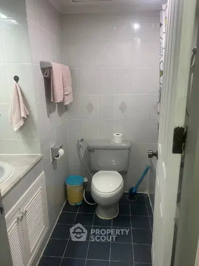 Compact bathroom with tiled walls and floor, featuring a toilet and sink.