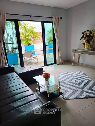 Modern living room with sleek black sofa and glass coffee table overlooking a lush garden patio.