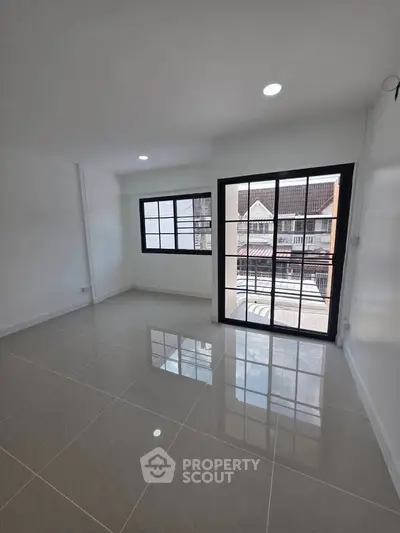 Bright living room with large windows and sliding glass door, offering ample natural light and modern tiled flooring.