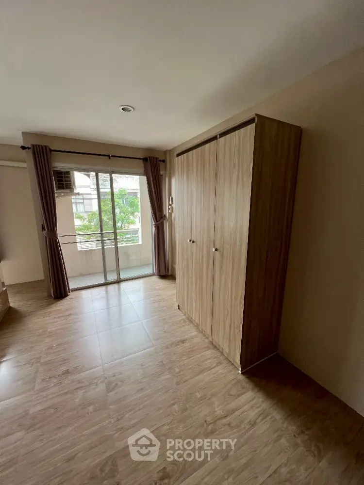 Spacious bedroom with wooden flooring and large window offering natural light and garden view.