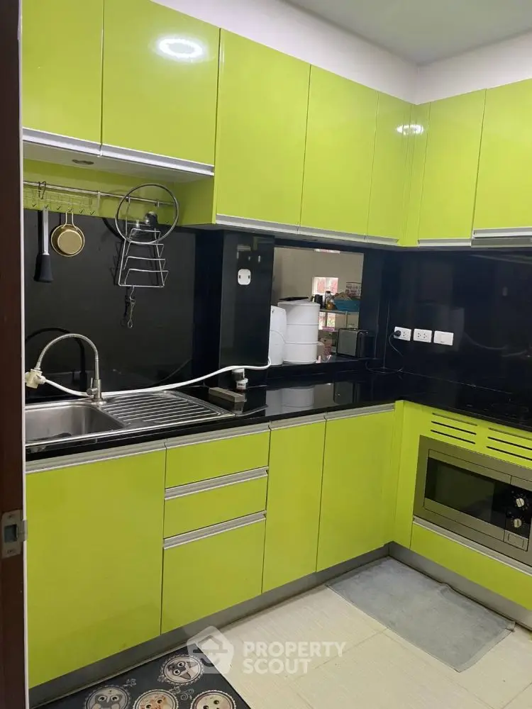 Modern kitchen with vibrant green cabinets and sleek black countertops.