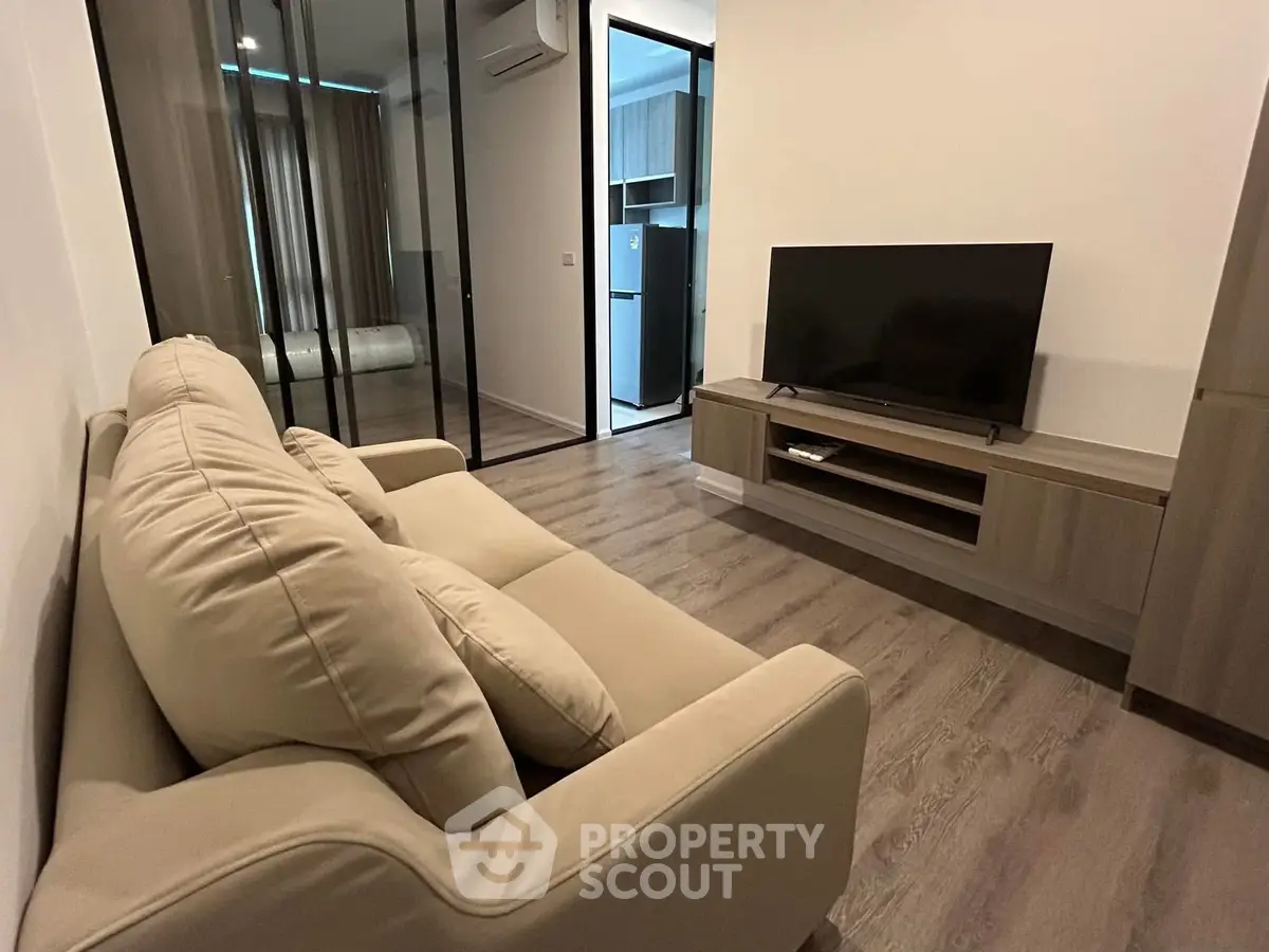 Modern living room with sleek design and glass partition, featuring a cozy sofa and flat-screen TV.