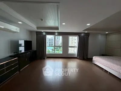 Spacious bedroom with large windows and city view, featuring modern furnishings and wooden flooring.