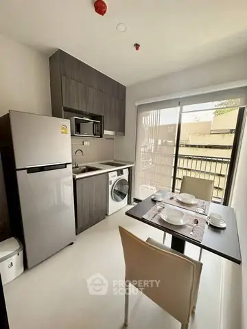 Modern kitchen with dining area, featuring fridge, microwave, washing machine, and sleek cabinetry.