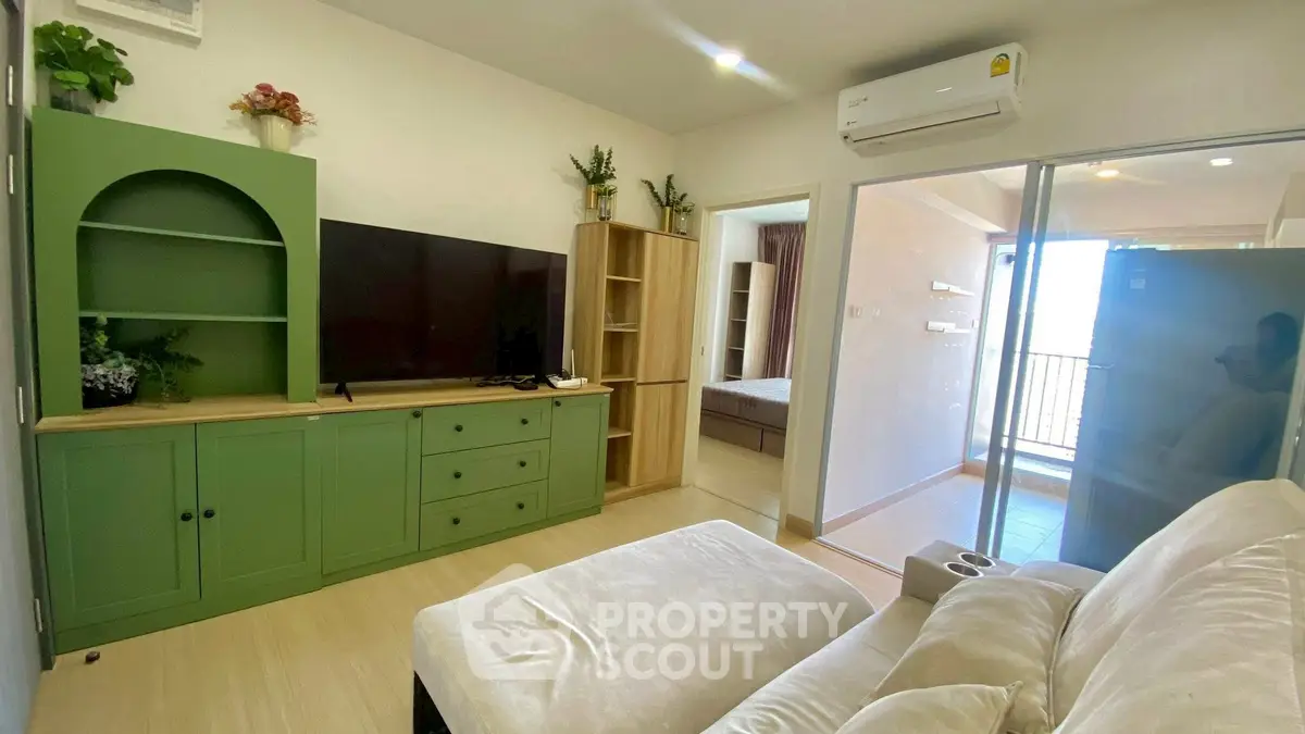 Charming living room with green cabinetry and cozy sofa, leading to a bedroom and balcony with natural light.