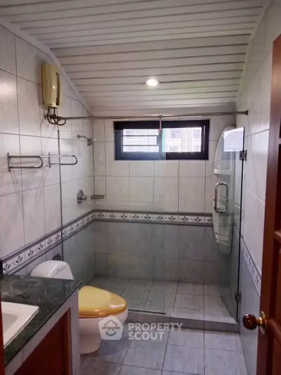 Charming bathroom with tiled walls, glass shower, and unique yellow toilet seat.