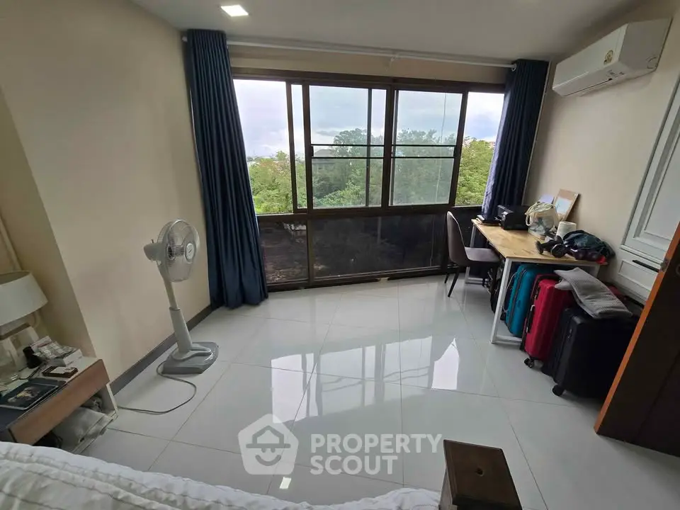 Bright bedroom with large window and scenic view, featuring modern furnishings and sleek tile flooring.