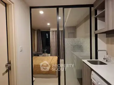 Modern studio apartment with glass partition, cozy bedroom, and compact kitchen area.
