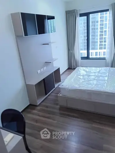 Modern bedroom with sleek furniture and large window offering city view, perfect for urban living.