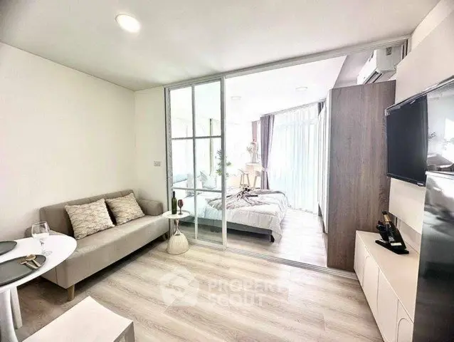 Modern open-plan living room with sliding glass doors to a bright bedroom, featuring sleek decor and natural light.