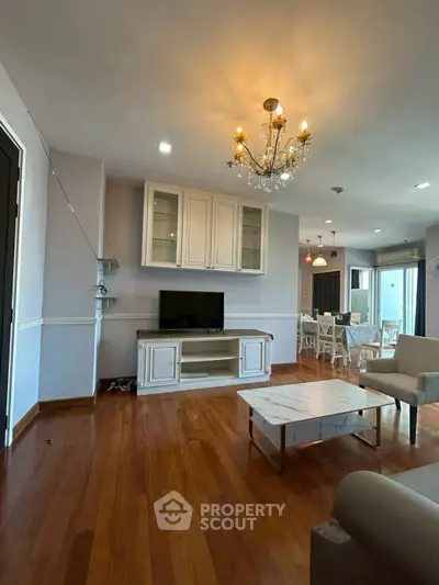 Spacious living room with elegant chandelier and hardwood floors in modern apartment