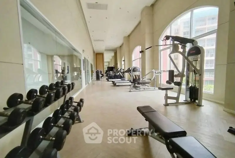 Spacious gym with modern equipment and large windows in luxury apartment building.