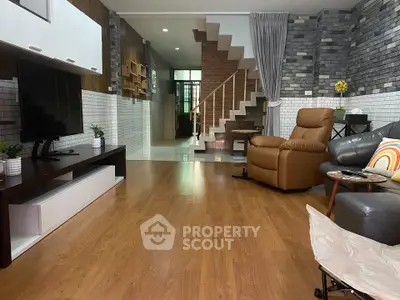 Spacious living room with modern decor and wooden flooring, featuring a cozy recliner and stylish staircase.