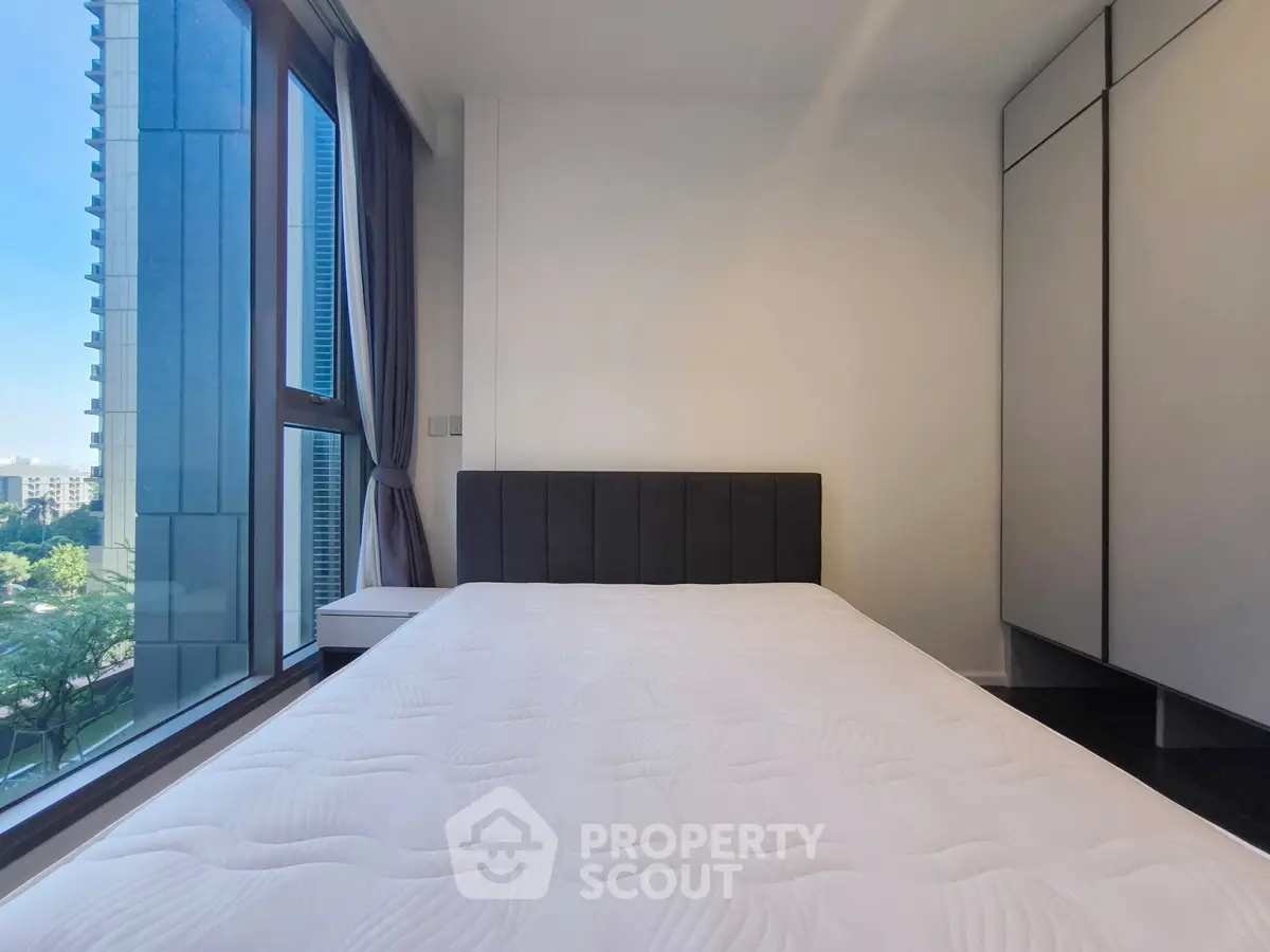 Modern bedroom with large window and built-in wardrobe in a high-rise apartment.