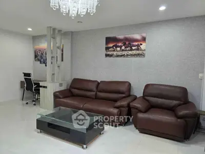Modern living room with leather sofas and glass coffee table, featuring elegant decor and ambient lighting.