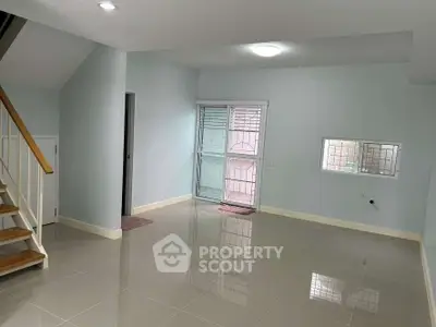 Spacious empty room with glossy tiled floor and staircase, ideal for customization.