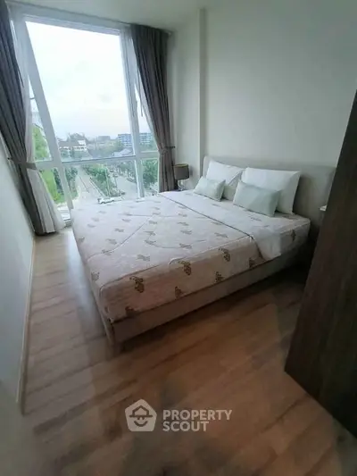 Modern bedroom with large windows and wooden flooring in a high-rise apartment.