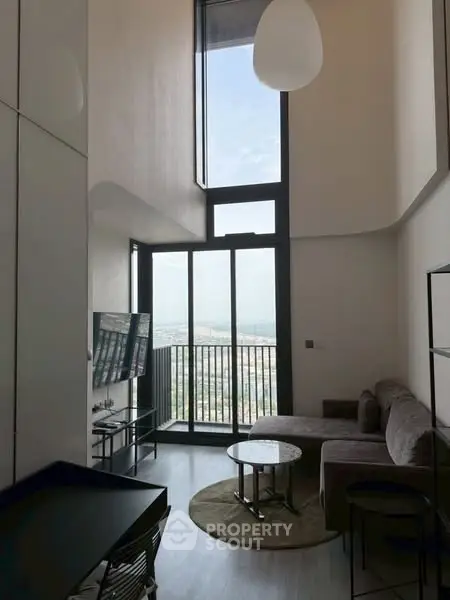 Modern living room with high ceiling and large windows offering stunning city views.