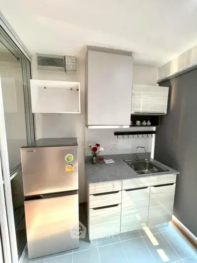Modern compact kitchen with stainless steel fridge and sleek cabinetry.