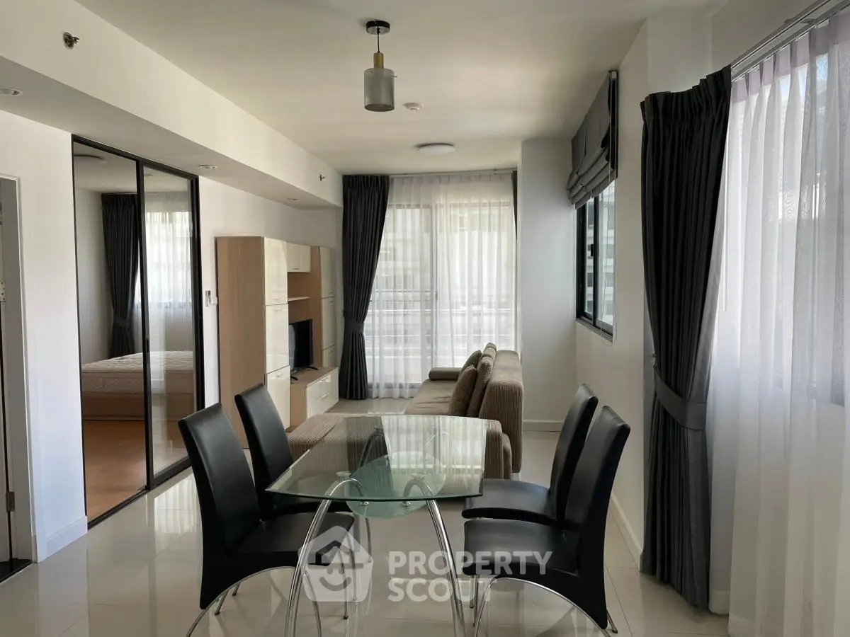 Modern open-plan living room with glass dining table and cozy seating area, featuring large windows and elegant curtains.