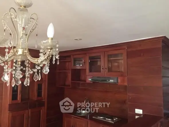 Elegant wooden kitchen with chandelier and modern appliances, perfect for stylish living.