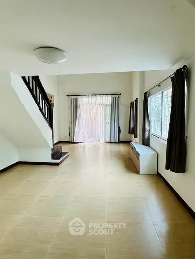 Spacious living room with natural light and modern staircase in a stylish home.