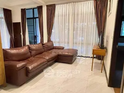 Spacious living room with elegant brown leather sofa and large windows with curtains.