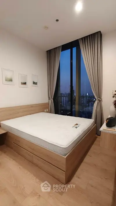 Modern bedroom with large window and city view, featuring wooden flooring and minimalist decor.