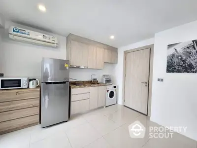 Modern kitchen with stainless steel fridge, microwave, and washing machine in sleek apartment.