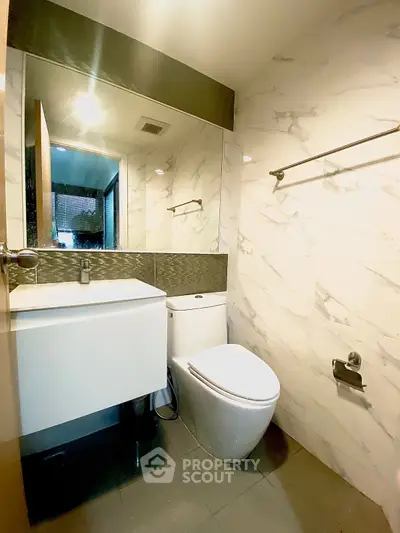 Modern bathroom with sleek fixtures and marble walls, featuring a large mirror and contemporary design.