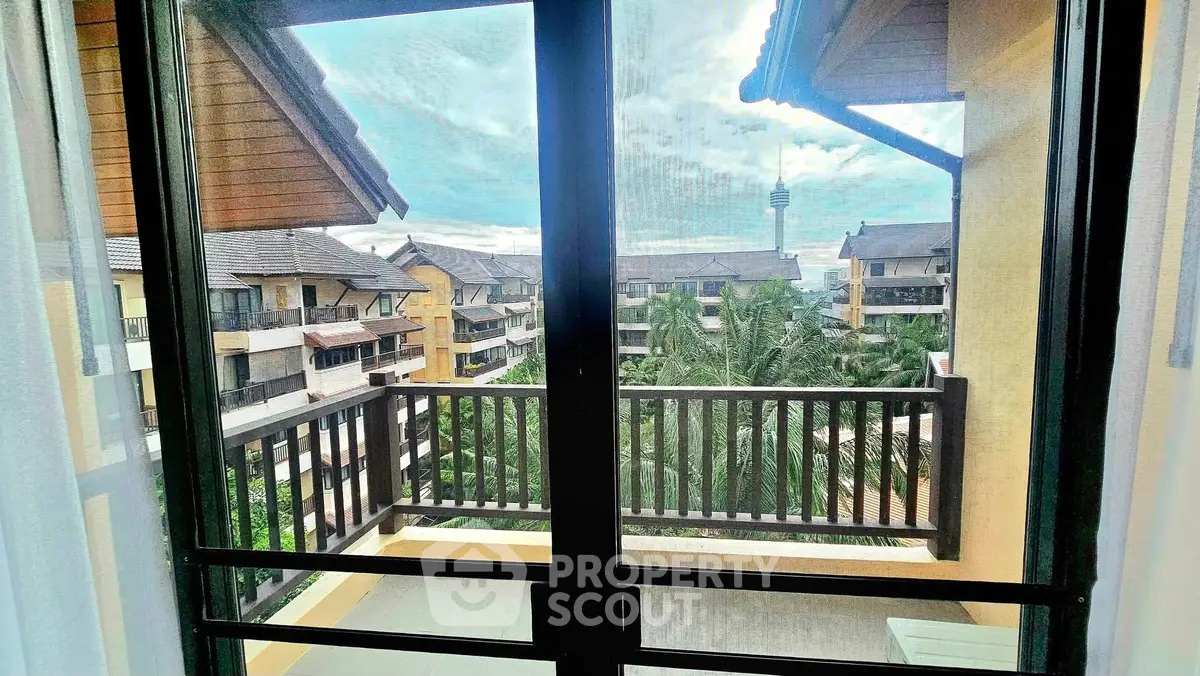 Stunning balcony view of tropical resort with lush greenery and distant tower.