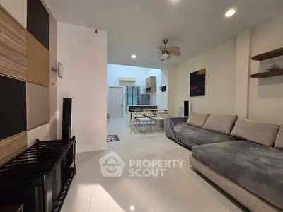 Modern living room with sleek furniture and open layout leading to dining area.