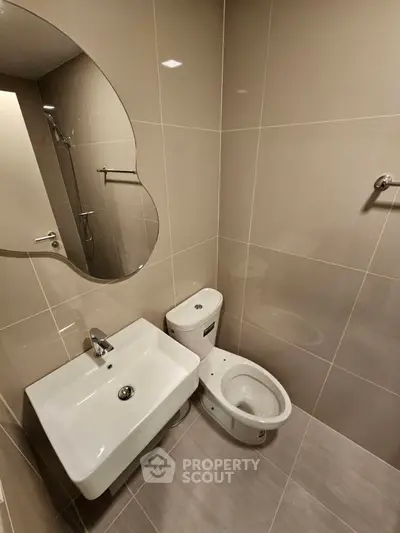 Modern bathroom with sleek fixtures and neutral tiles, featuring a stylish sink and toilet.
