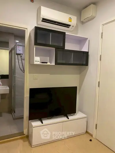 Modern living room with sleek TV unit and air conditioning, adjacent to a bathroom.