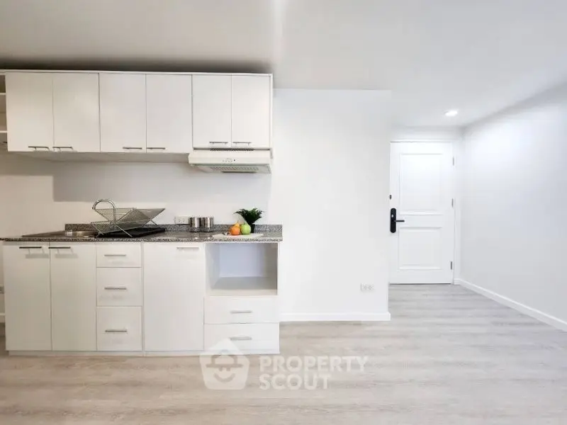 Modern minimalist kitchen with sleek white cabinets and light wood flooring.