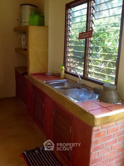 Charming rustic kitchen with brick accents and lush garden view, featuring a spacious countertop and open shelving.