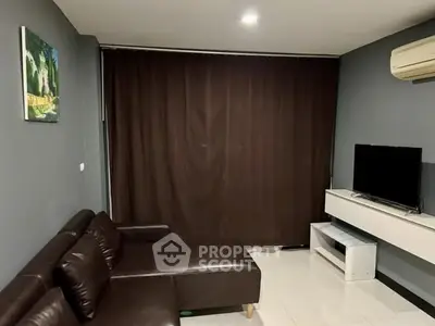 Modern living room with dark leather sofa and wall-mounted TV, featuring sleek design and cozy ambiance.