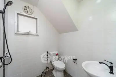 Modern bathroom with sleek fixtures and white tiles, featuring a compact design under a sloped ceiling.