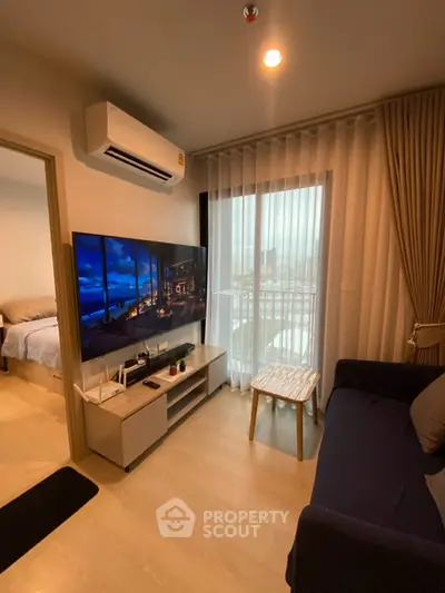 Modern living room with large TV, cozy sofa, and natural light from window.