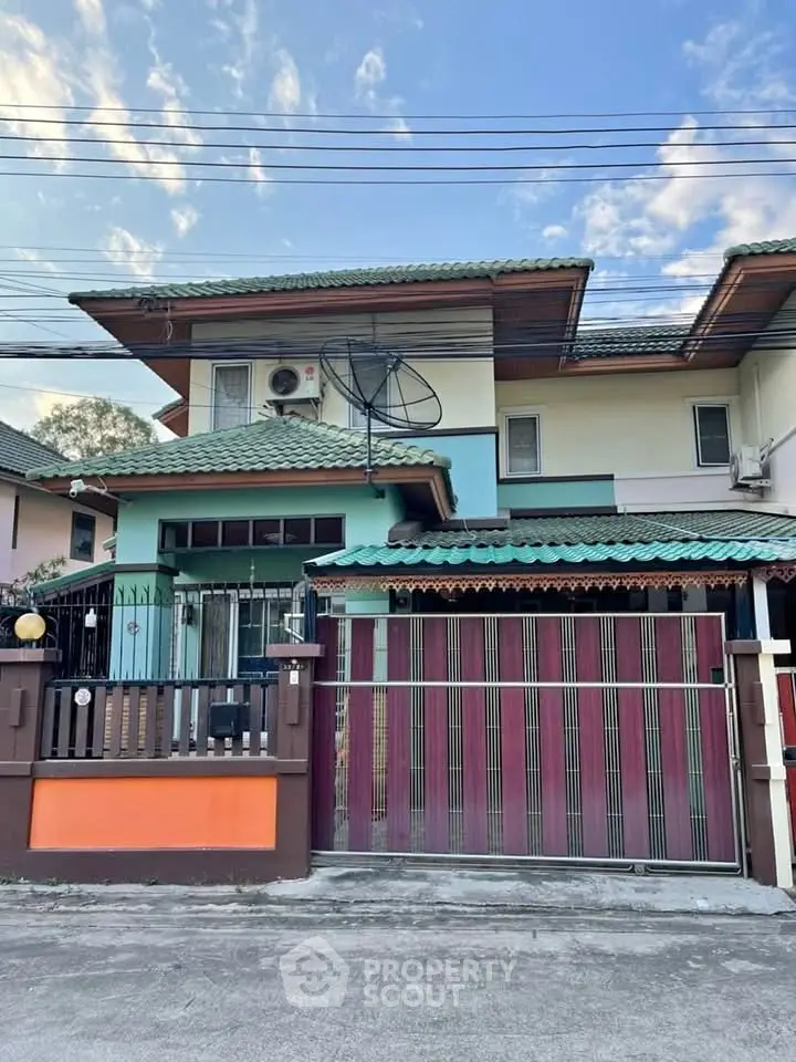 Charming two-story house with green roof and gated entrance in a serene neighborhood.